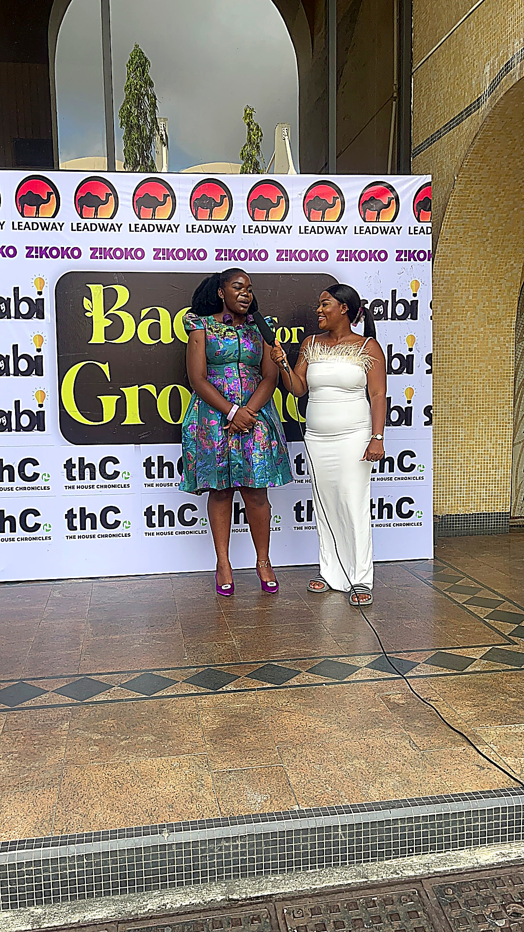 Ibi Kontein being interviewed in front of a Back For Ground step-and-repeat banner in Lagos, speaking to a presenter holding a microphone.